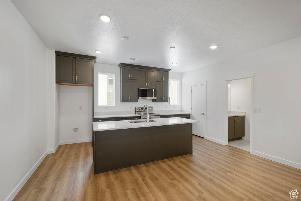 Kitchen with stainless steel appliances, light countertops, light wood finished floors, baseboards, and a center island with sink