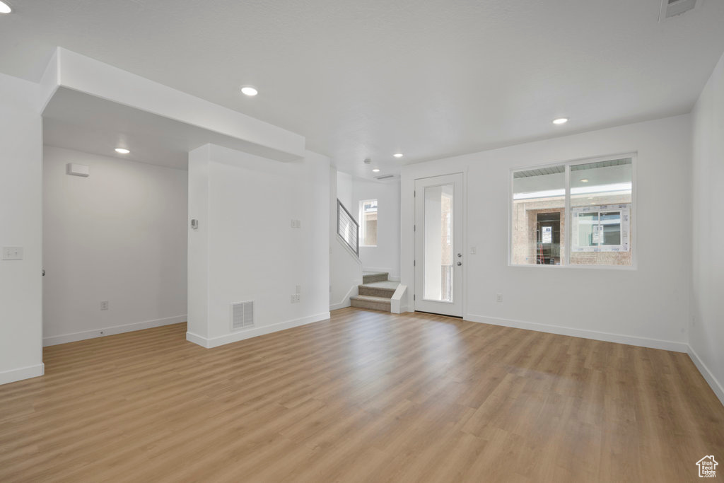 Unfurnished living room featuring light wood-style flooring, stairs, recessed lighting, and baseboards