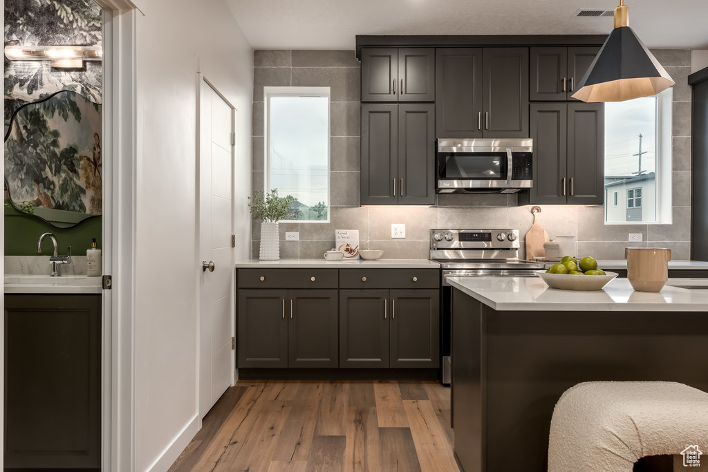 Kitchen with appliances with stainless steel finishes, a sink, wood finished floors, light countertops, and decorative backsplash