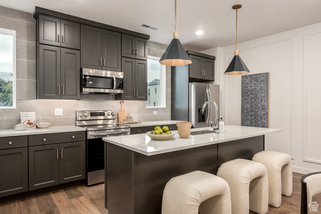 Kitchen with stainless steel appliances, a sink, light countertops, light wood-type flooring, and tasteful backsplash