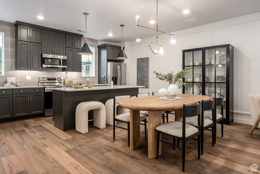 Kitchen featuring appliances with stainless steel finishes, light countertops, wood finished floors, a kitchen island with sink, and recessed lighting