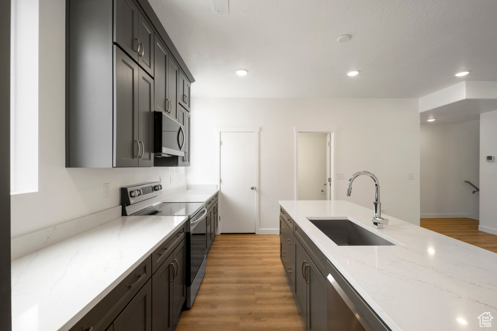Kitchen with stainless steel appliances, a sink, light wood-style floors, light stone countertops, and recessed lighting