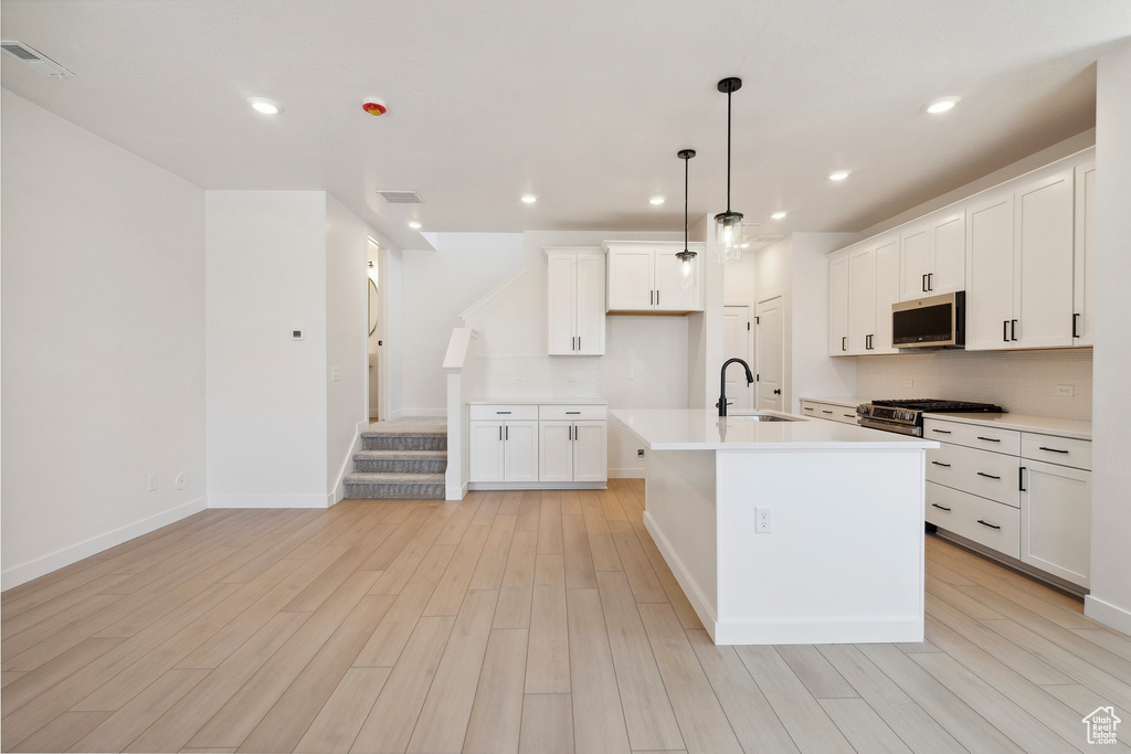 Kitchen with stainless steel appliances, a sink, light wood-style flooring, a kitchen island with sink, and light countertops