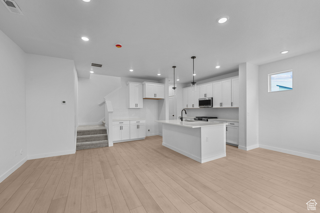 Kitchen with stainless steel microwave, a center island with sink, light countertops, baseboards, and white cabinetry