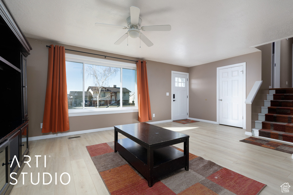Living room featuring light wood-style floors, ceiling fan, stairway, and baseboards