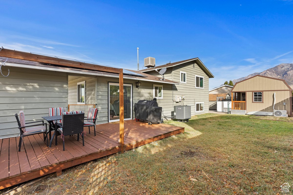 Back of property featuring outdoor dining area, roof mounted solar panels, a lawn, a deck, and central AC