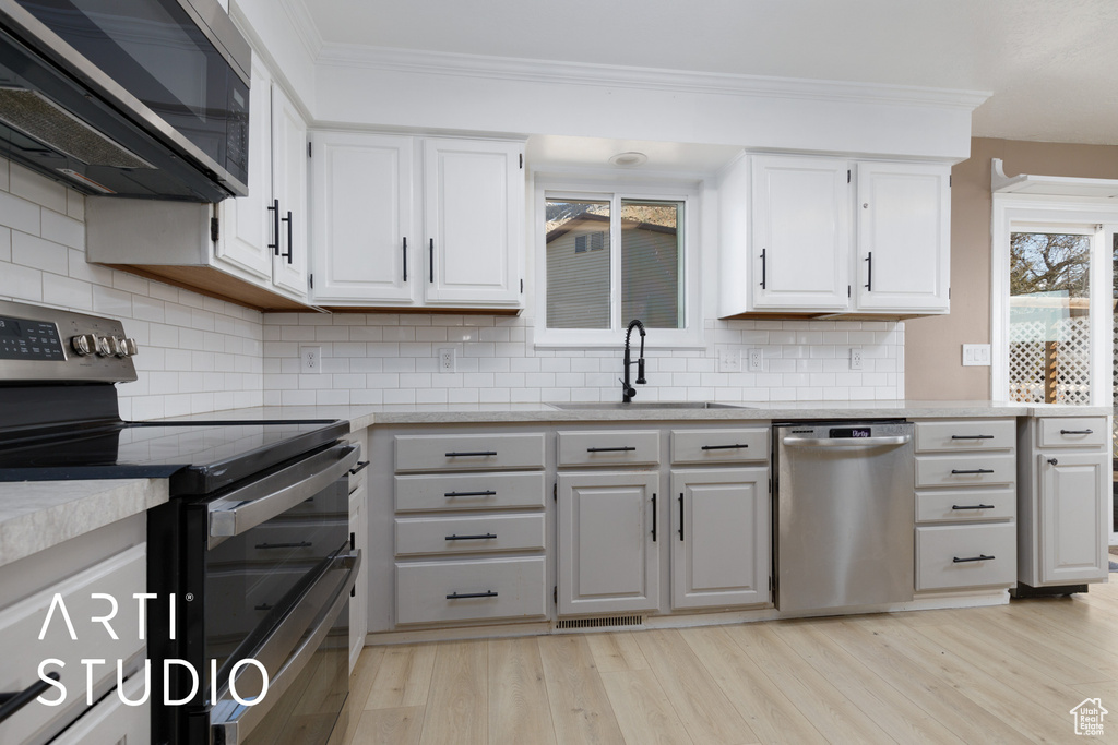 Kitchen featuring appliances with stainless steel finishes, a sink, ornamental molding, white cabinets, and light countertops