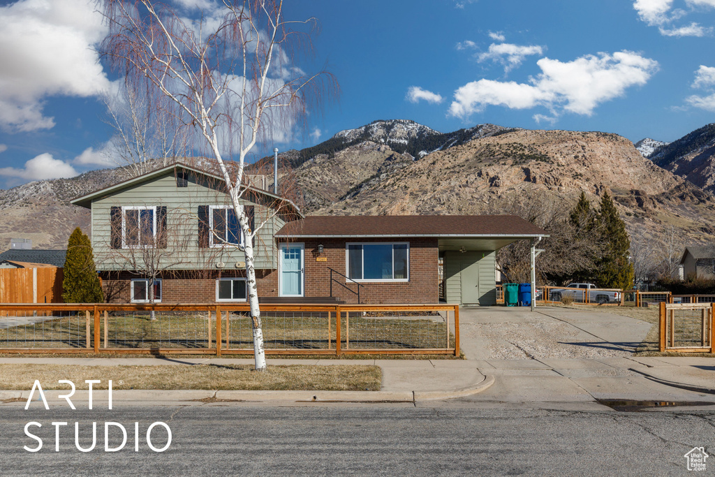View of front of house with driveway, a mountain view, a fenced front yard, and an attached carport