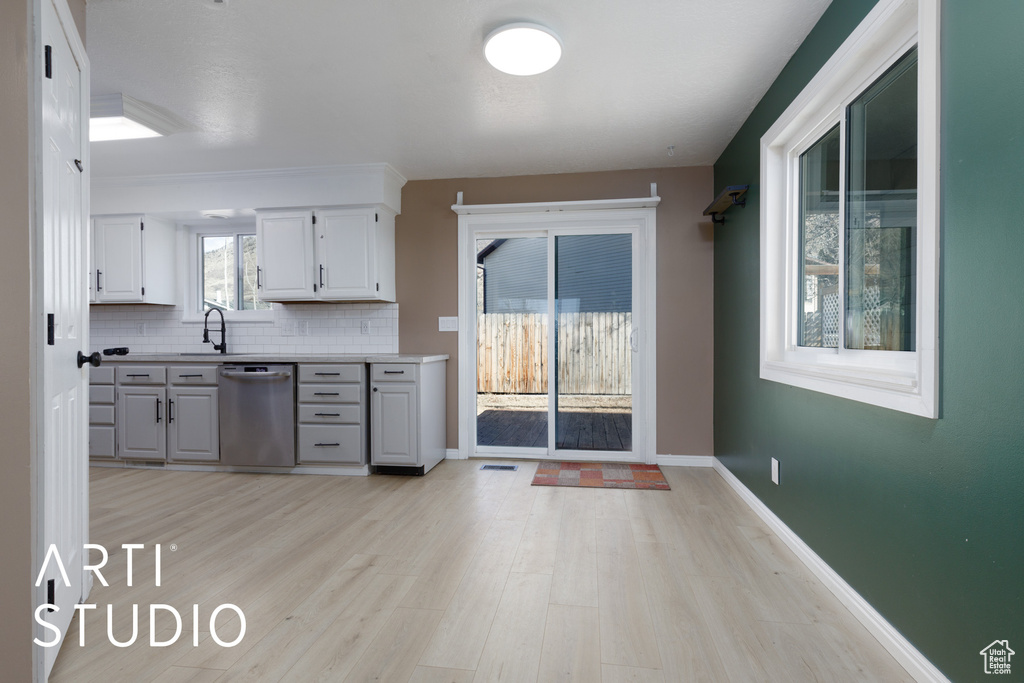 Kitchen featuring stainless steel dishwasher, light wood-style floors, light countertops, a sink, and tasteful backsplash