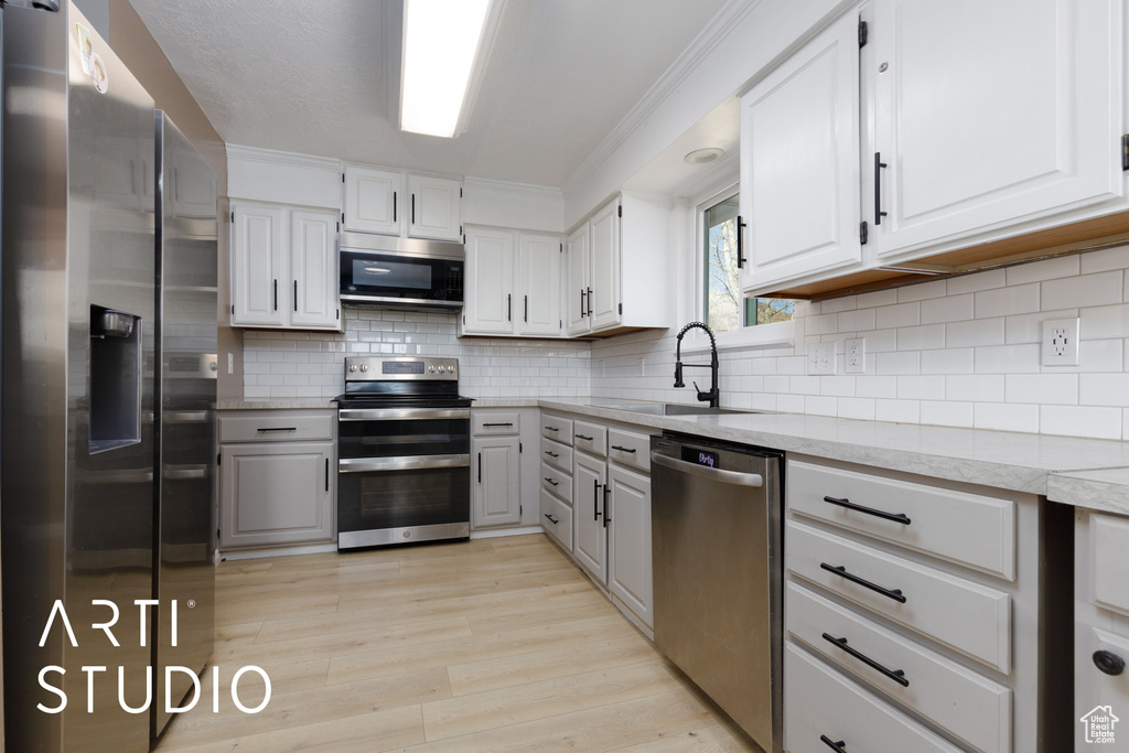 Kitchen featuring appliances with stainless steel finishes, a sink, gray cabinetry, light wood-style floors, and backsplash