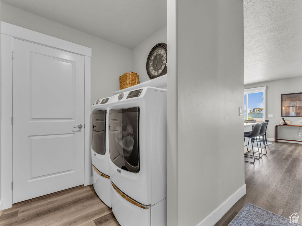 Laundry area featuring washing machine and dryer, light wood-style floors, baseboards, and a textured ceiling