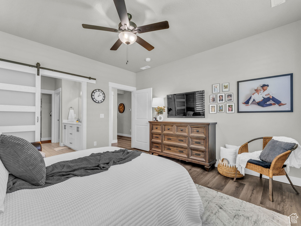 Bedroom with a barn door, wood finished floors, baseboards, and a ceiling fan