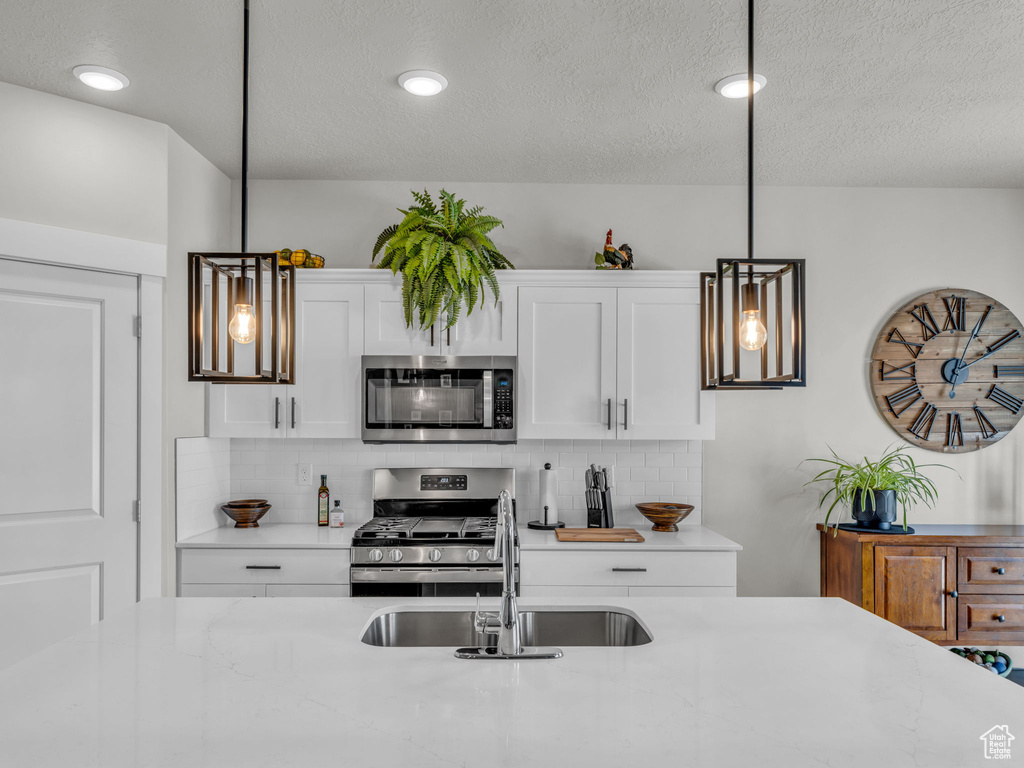 Kitchen with stainless steel appliances, a sink, decorative backsplash, white cabinetry, and a textured ceiling