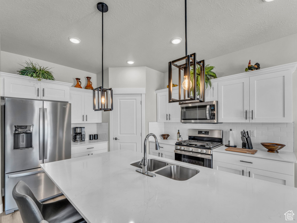 Kitchen with appliances with stainless steel finishes, a sink, a textured ceiling, backsplash, and light countertops