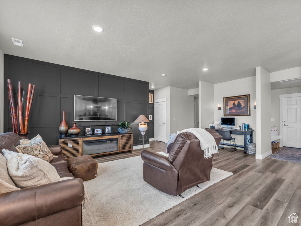 Living area with wood finished floors, a decorative wall, baseboards, and recessed lighting