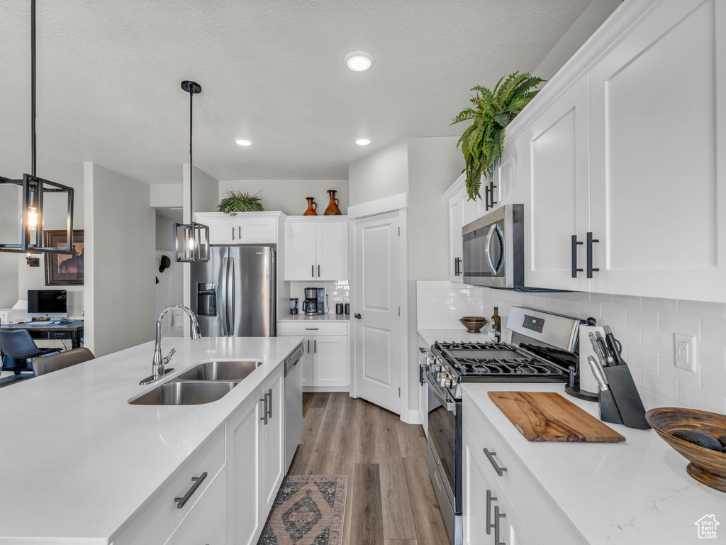 Kitchen featuring stainless steel appliances, a sink, light countertops, white cabinetry, and wood finished floors