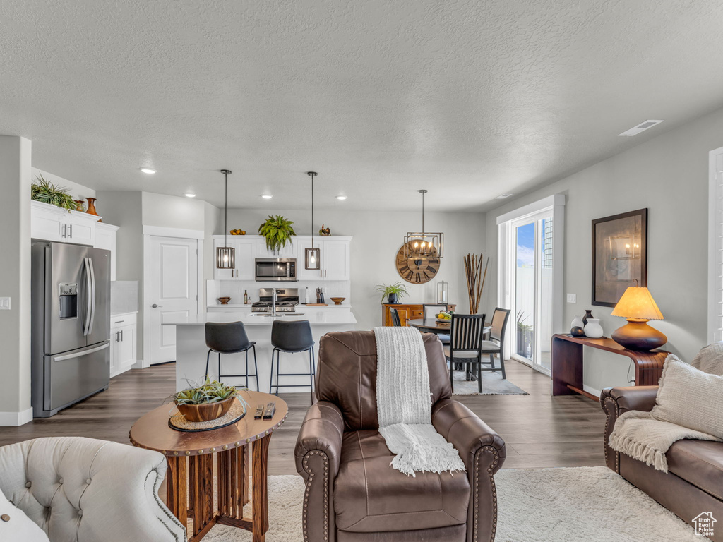 Living room featuring dark wood finished floors, a chandelier, a textured ceiling, and recessed lighting