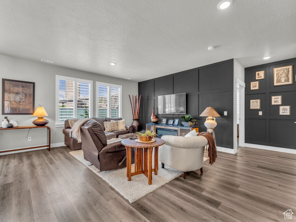 Living room with a textured ceiling, light wood-type flooring, baseboards, recessed lighting, and a decorative wall