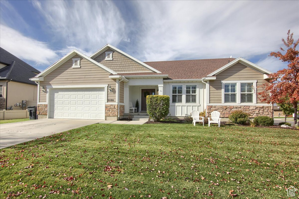 View of front of property with stone siding, driveway, a front yard, and a garage