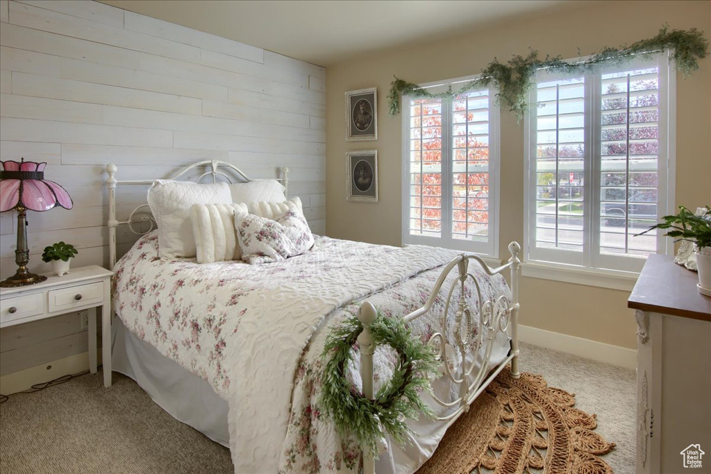 Bedroom featuring light carpet, multiple windows, and wood walls