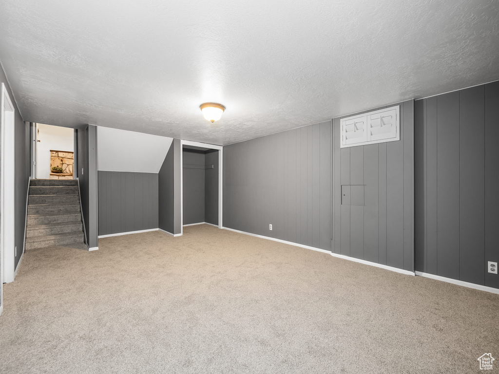 Finished below grade area featuring a textured ceiling, carpet floors, stairway, and baseboards