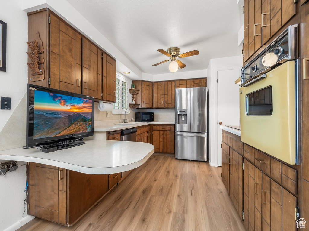 Kitchen featuring stainless steel appliances, a peninsula, light countertops, light wood-style floors, and ceiling fan