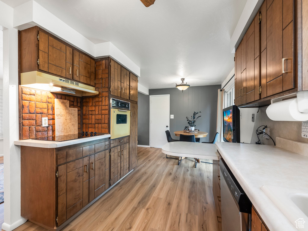 Kitchen featuring oven, dishwasher, light wood-type flooring, light countertops, and black electric cooktop