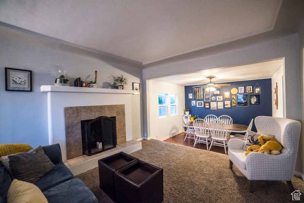 Carpeted living room featuring a ceiling fan, a tiled fireplace, and baseboards