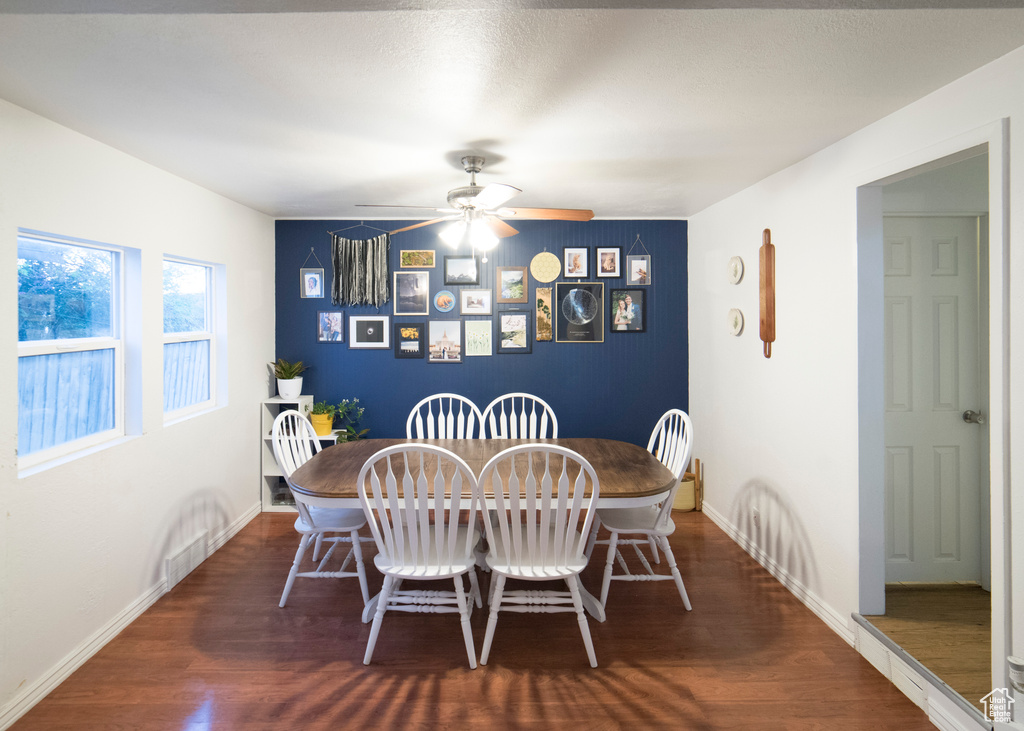 Dining area with an accent wall, wood finished floors, baseboards, and a ceiling fan