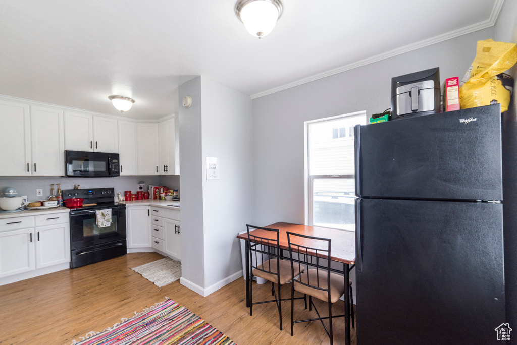 Kitchen with black appliances, light wood finished floors, white cabinetry, light countertops, and ornamental molding