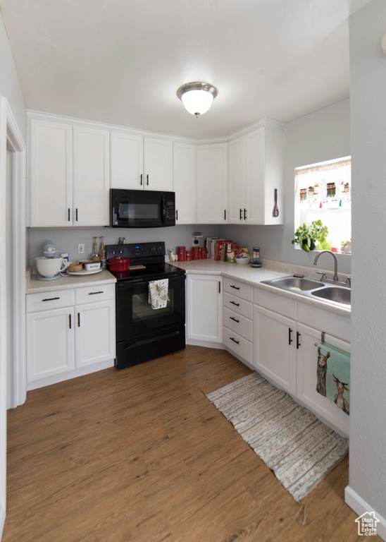 Kitchen featuring black appliances, a sink, white cabinets, and wood finished floors