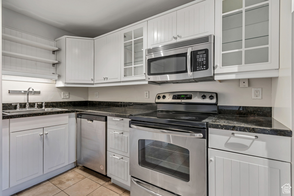 Kitchen featuring appliances with stainless steel finishes, a sink, open shelves, light tile patterned floors, and white cabinetry