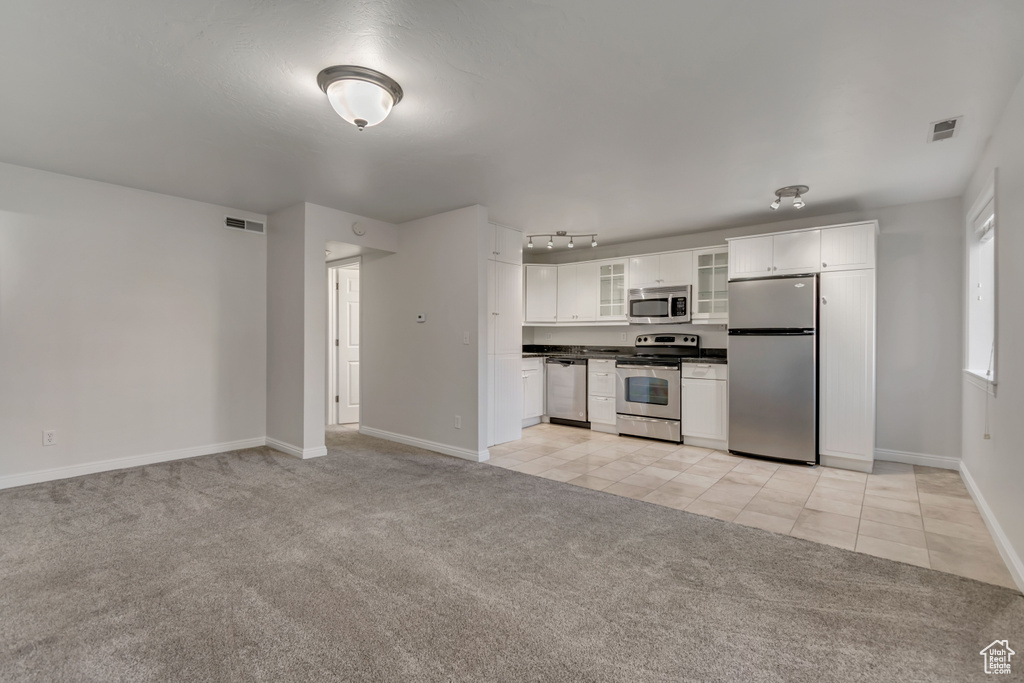 Kitchen featuring stainless steel appliances, light carpet, dark countertops, glass insert cabinets, and white cabinets