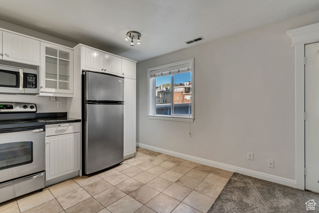 Kitchen with appliances with stainless steel finishes, glass insert cabinets, dark countertops, white cabinetry, and light tile patterned floors