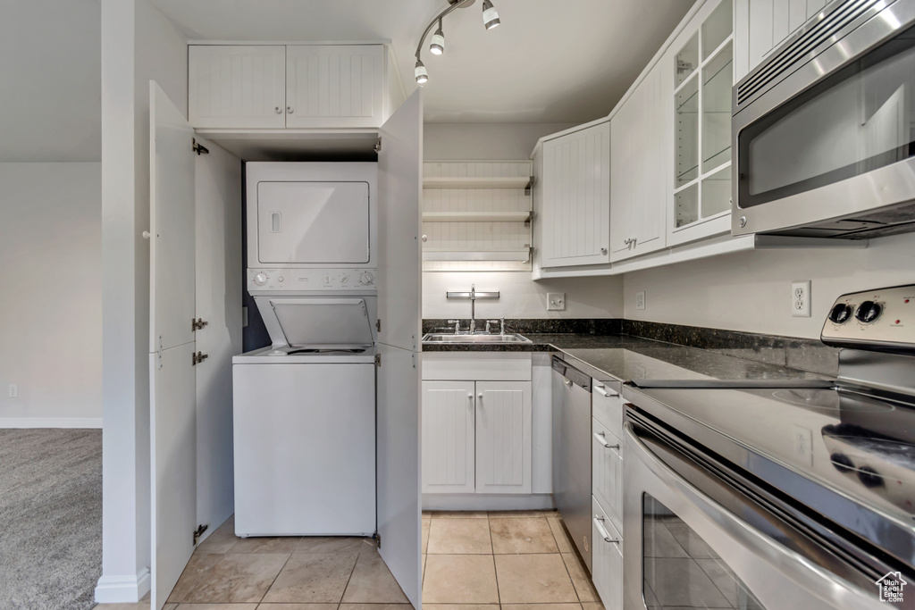 Kitchen featuring appliances with stainless steel finishes, estacked washer and dryer, a sink, white cabinets, and glass insert cabinets