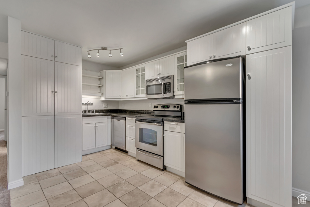 Kitchen featuring appliances with stainless steel finishes, dark countertops, open shelves, a sink, and light tile patterned floors