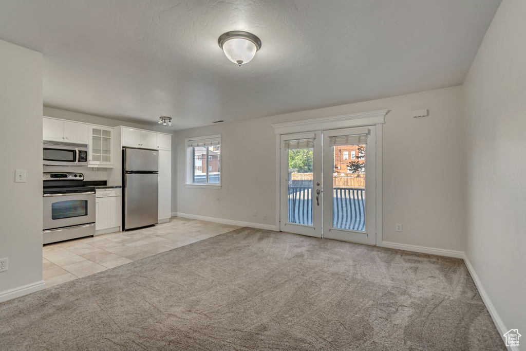 Kitchen with stainless steel appliances, light colored carpet, glass insert cabinets, white cabinetry, and baseboards