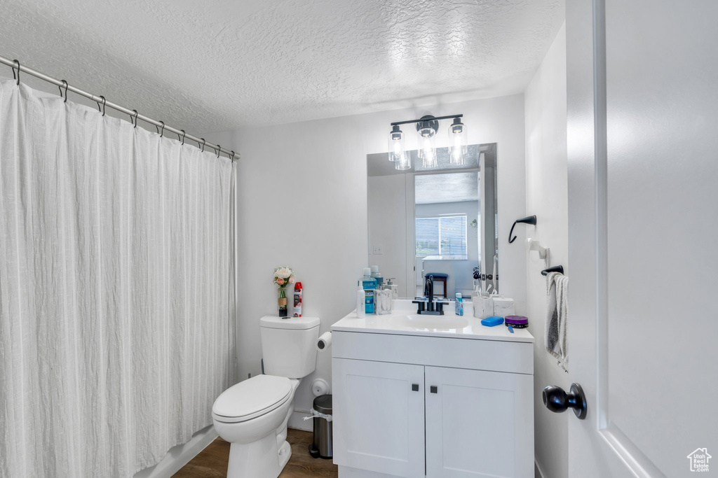 Bathroom featuring a textured ceiling, toilet, vanity, wood finished floors, and a shower with curtain