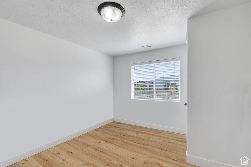 Spare room featuring baseboards, light wood finished floors, and a textured ceiling