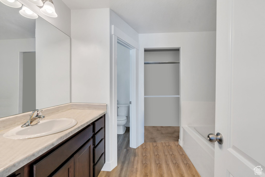 Full bath with toilet, vanity, wood finished floors, and a bath