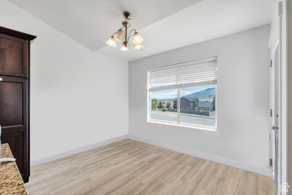 Unfurnished dining area with a chandelier, light wood-style flooring, and baseboards