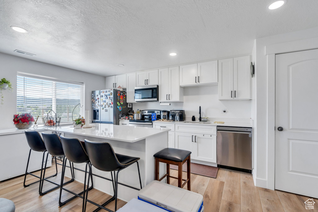 Kitchen with appliances with stainless steel finishes, a sink, a kitchen breakfast bar, white cabinets, and light countertops