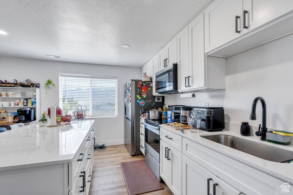 Kitchen featuring appliances with stainless steel finishes, a sink, recessed lighting, white cabinets, and a textured ceiling