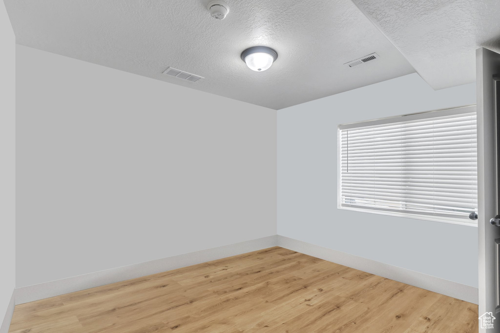 Spare room with a textured ceiling, a smoke detector, light wood-type flooring, and baseboards