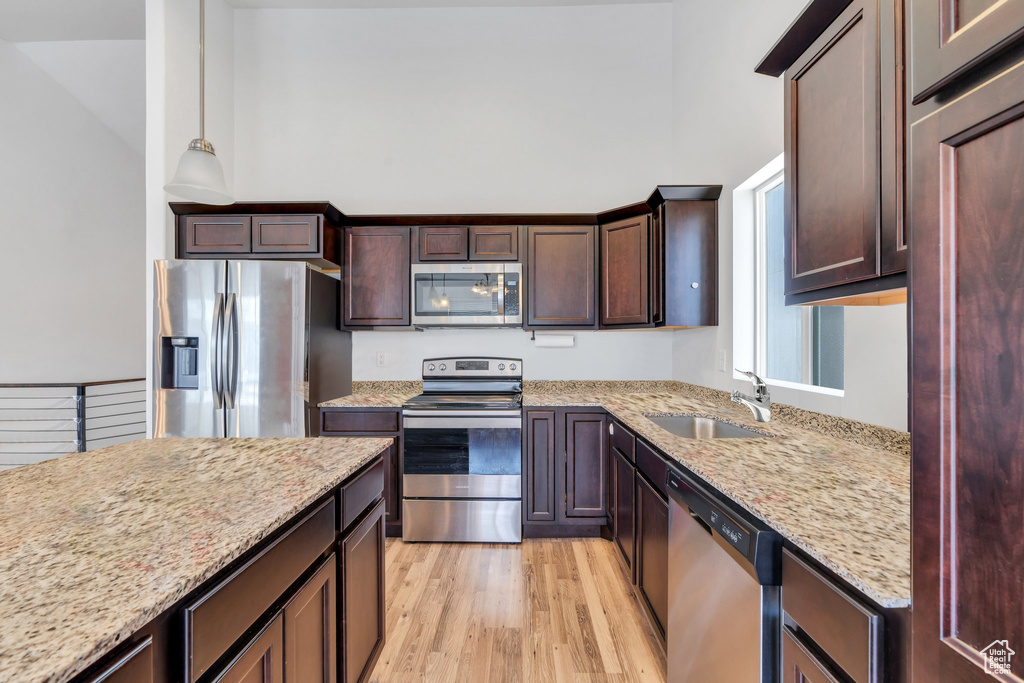 Kitchen with appliances with stainless steel finishes, a sink, light stone counters, light wood finished floors, and dark brown cabinets