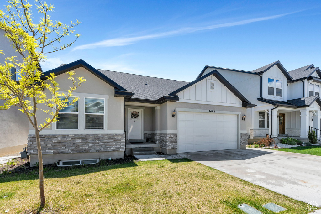 View of front of property featuring stone siding, board and batten siding, driveway, and a front lawn