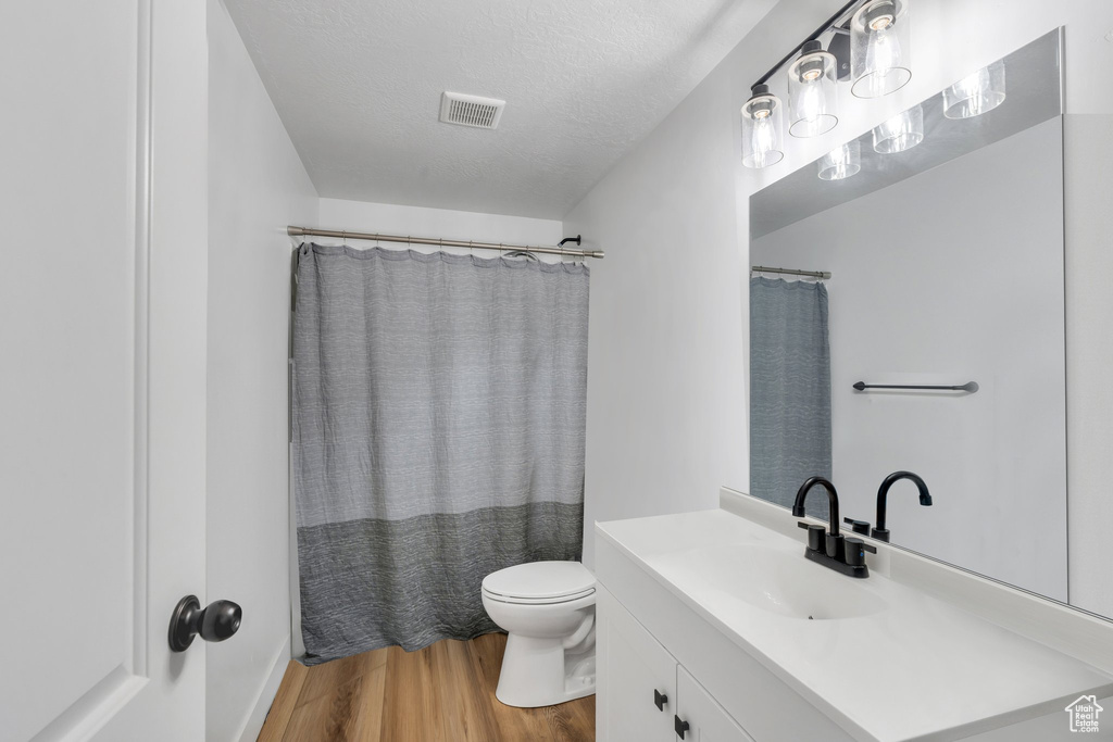 Bathroom with wood finished floors, toilet, vanity, a textured ceiling, and a shower with curtain