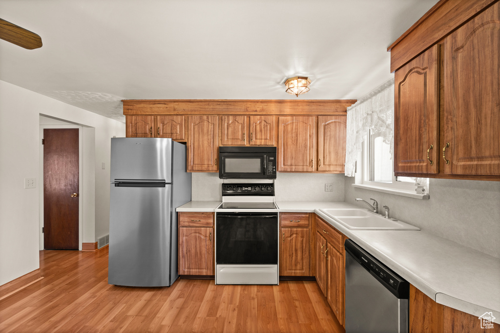 Kitchen featuring appliances with stainless steel finishes, a sink, brown cabinets, and light countertops