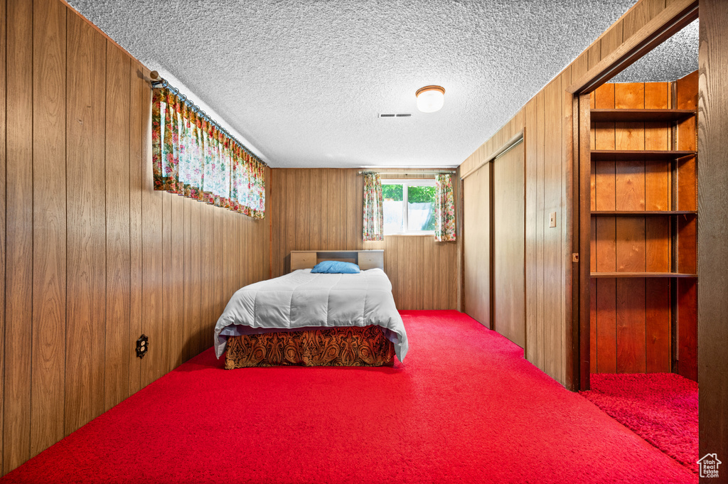Bedroom with wooden walls, carpet flooring, a closet, and a textured ceiling