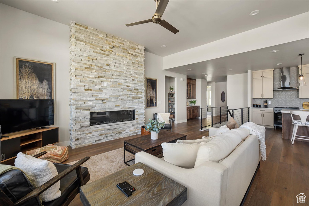 Living room with a ceiling fan, a stone fireplace, dark wood-style floors, recessed lighting, and baseboards